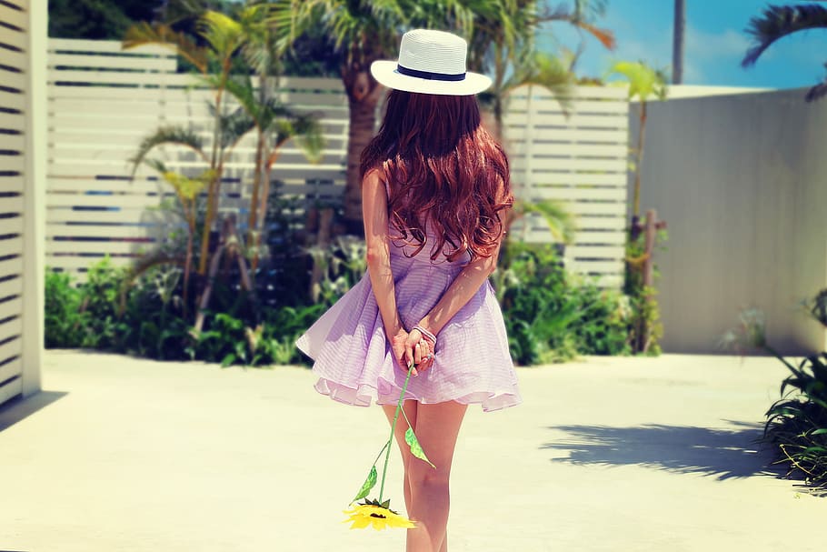 brunette hair girl in purple dress holding sunflower while walking on grey ground