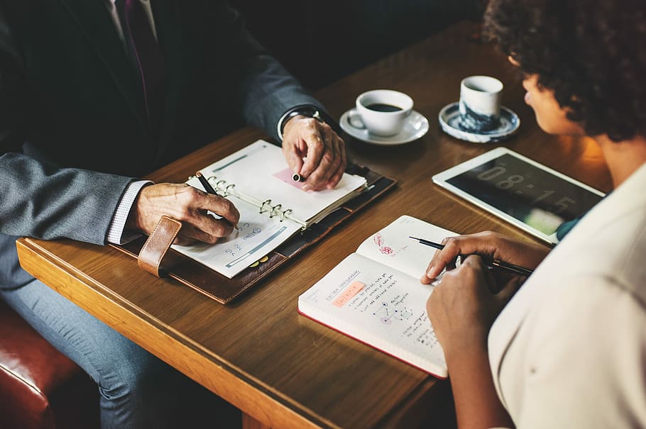 two people sitting next to table writing on notebooks, coffee HD wallpaper