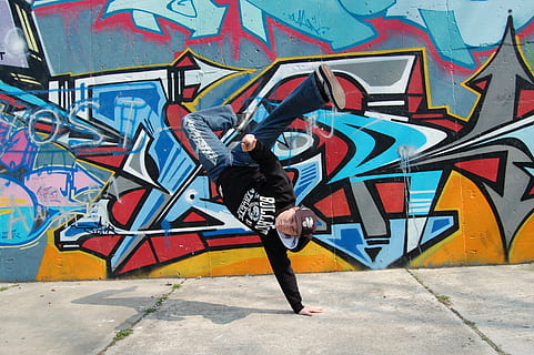 man wears black hoodie doing one hand stand near multicolored wall graffiti during daytime HD wallpaper