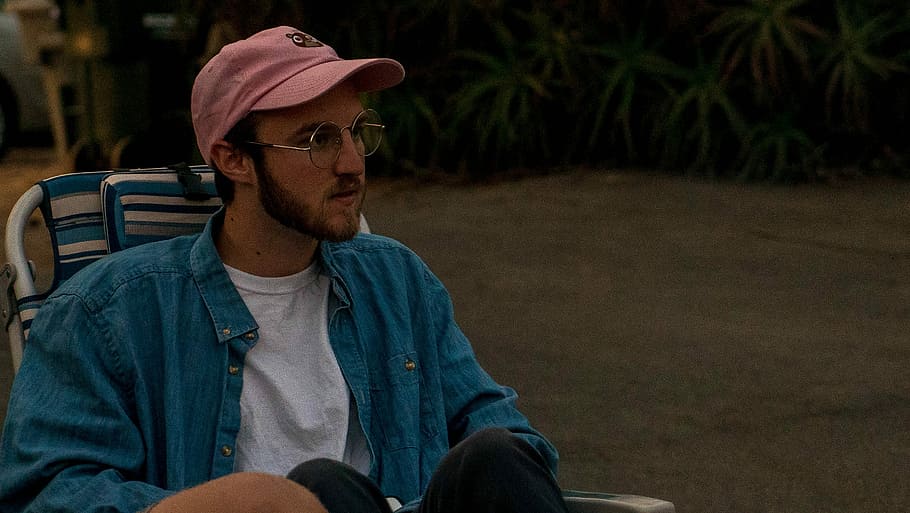 man sitting on chair, man sitting on lounger chair wearing blue jacket and pink cap outdoor HD wallpaper