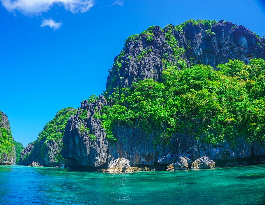 body of water beside mountain and trees under blue and white sky at daytime, gray rock formation covered with green plants HD wallpaper