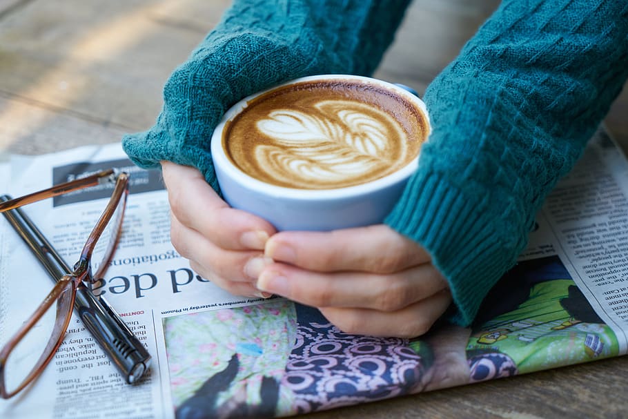 woman wearing blue sweater holding white coffee mug with espresso