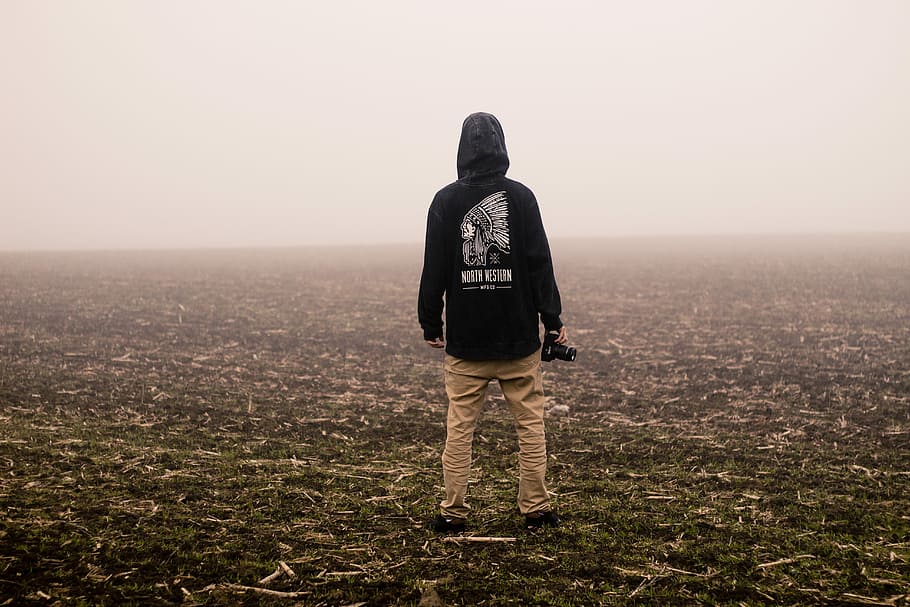 person holding a camera standing on grass field, man wearing black hoodie while standing on plain, HD wallpaper