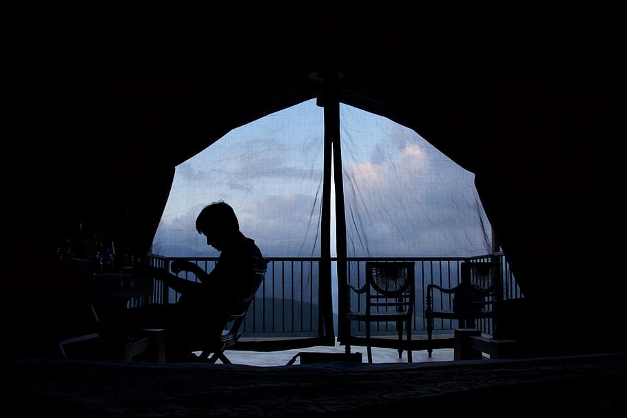 person sitting on chair inside canopy tent, silhouette of man sitting on chair at daytime