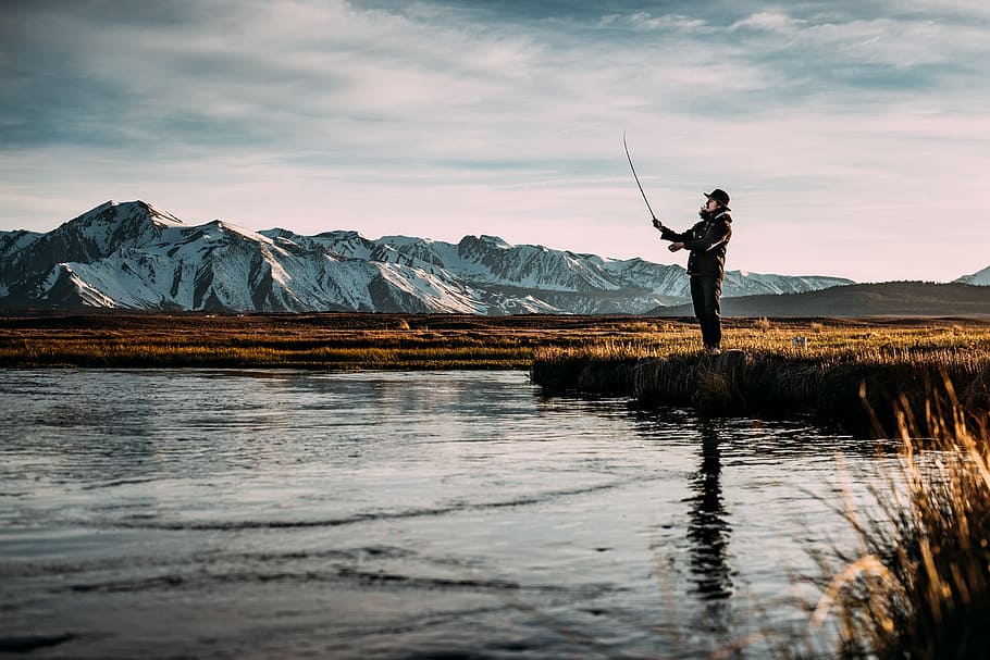 landscape photo of man fishing on river near mountain alps, man stands near body of water HD wallpaper