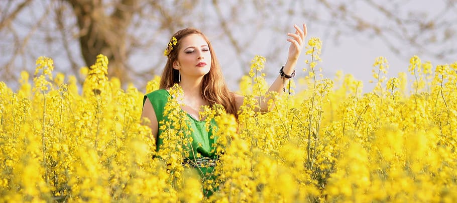 woman wearing green scoop-neck sleeveless top surrounded by yellow flowers