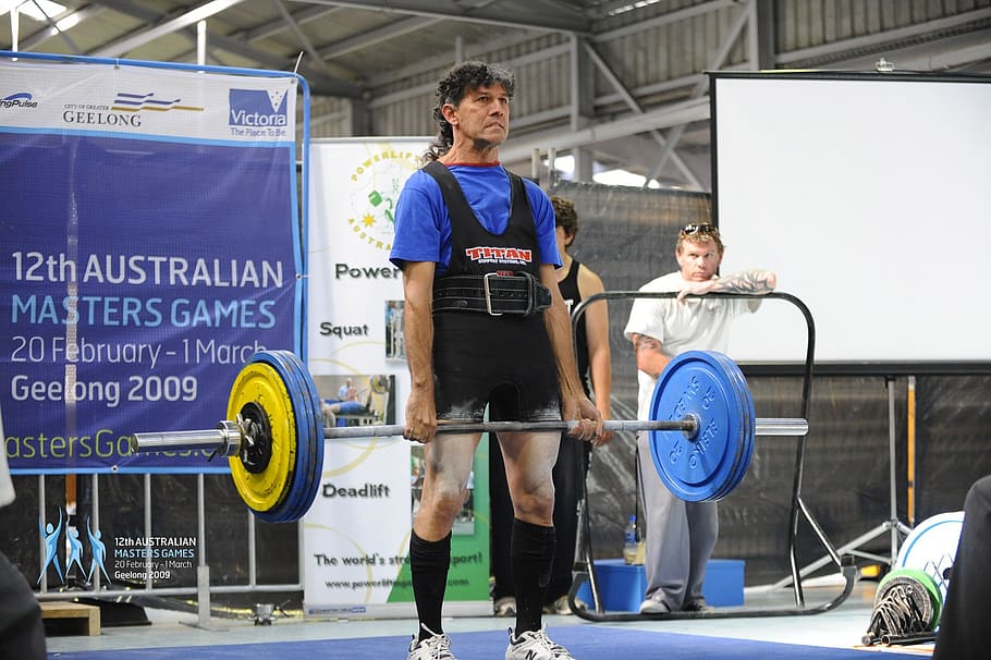 man in black top carrying yellow and blue barbells, deadlift
