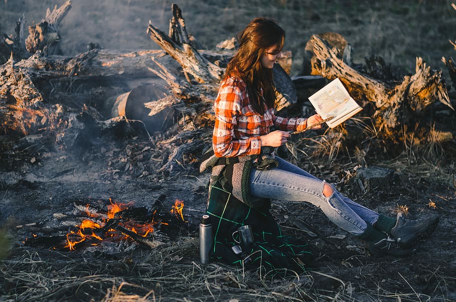 woman sitting while reading near bonfire, shallow focus photography of woman near bonfire reading book HD wallpaper