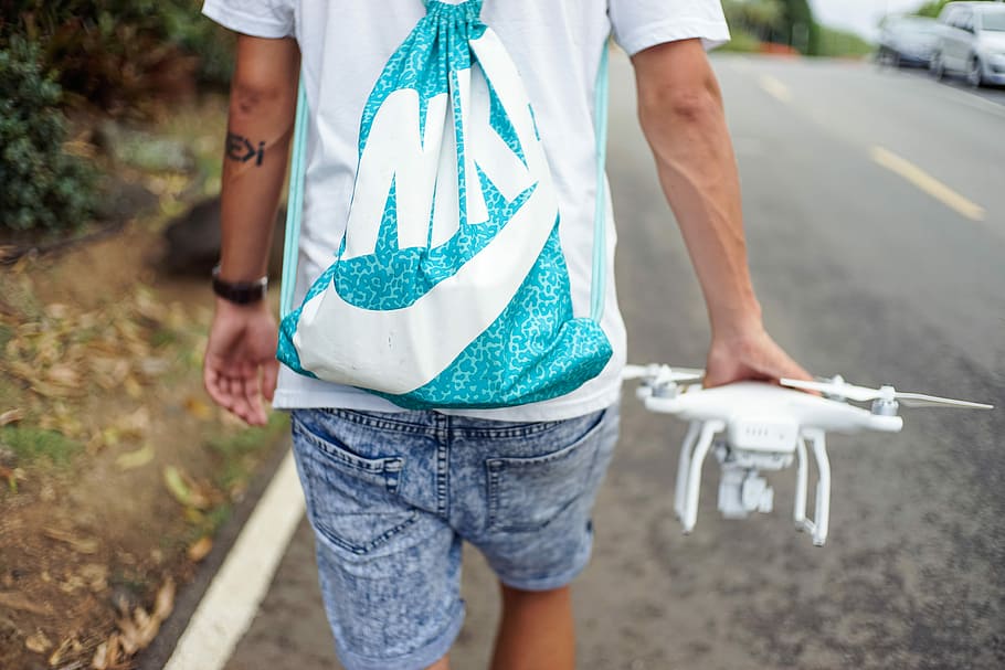 man holding white R/C quadcopter while walking beside concrete roadway, person carrying white quadcopter drone while walking on street during daytime HD wallpaper