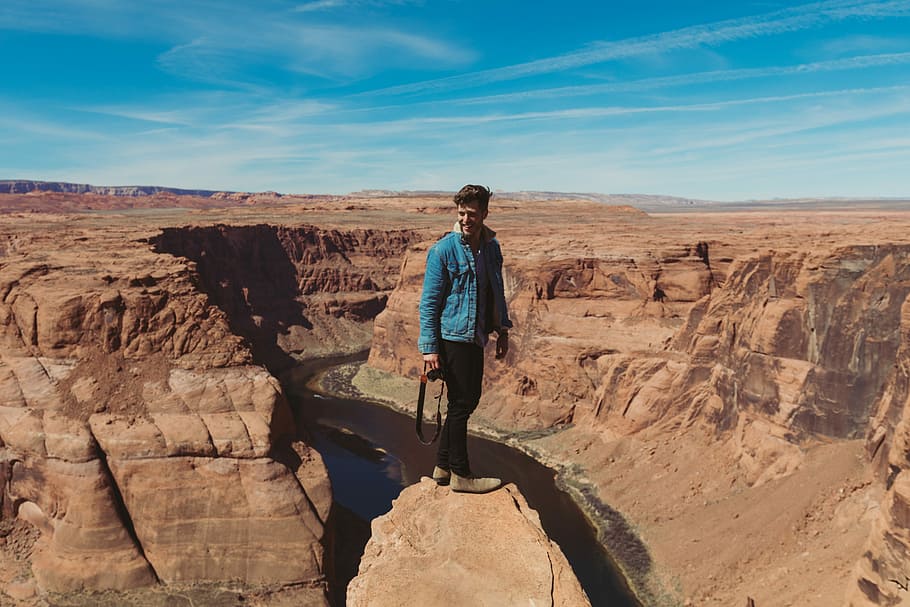 man standing on rocky cliff across hills during daytime, man standing on rock formation HD wallpaper