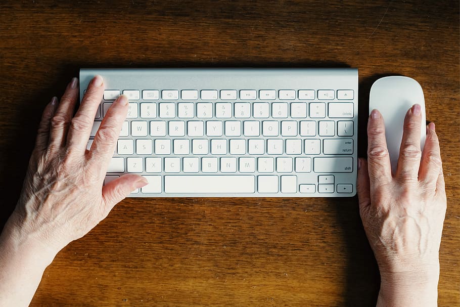 person holding white computer mouse and keyboard on brown wooden board HD wallpaper