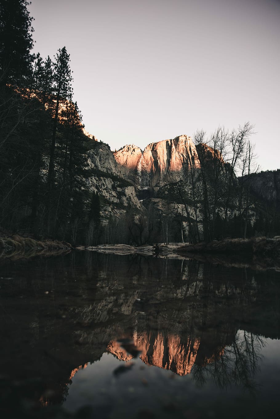 rock formation surrounded with trees, body of water across snow covered mountain HD wallpaper