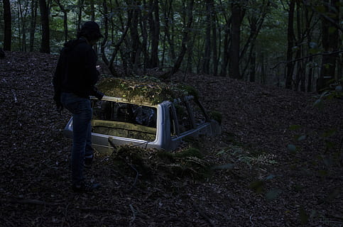 landscape photography of man standing in front of half-buried broken car at forest, white camping shell HD wallpaper