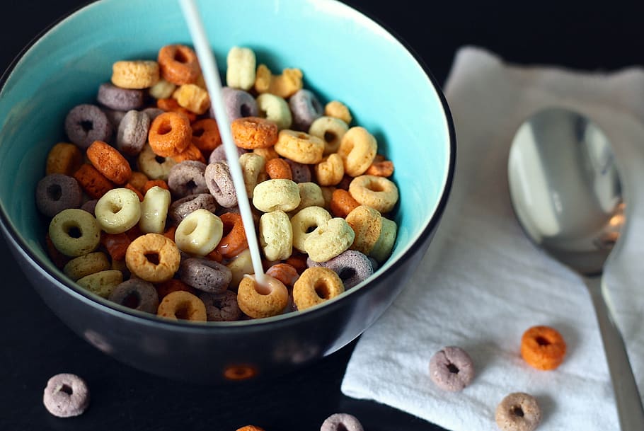 milk poured onto cereals in bowl next to spoon, cheerios, children