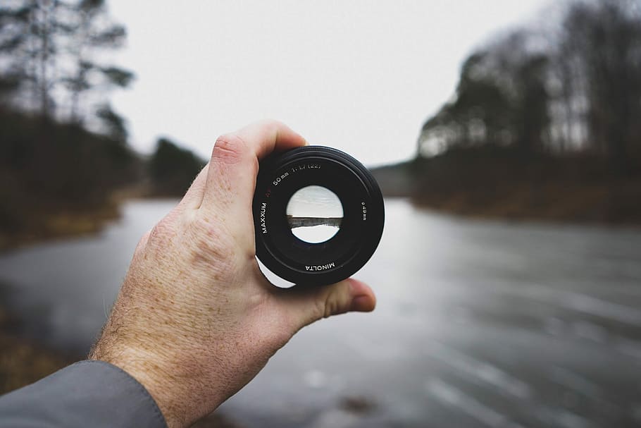 selective focus photo of person's hand holding black camera lens, photo of person holding black camera lens HD wallpaper
