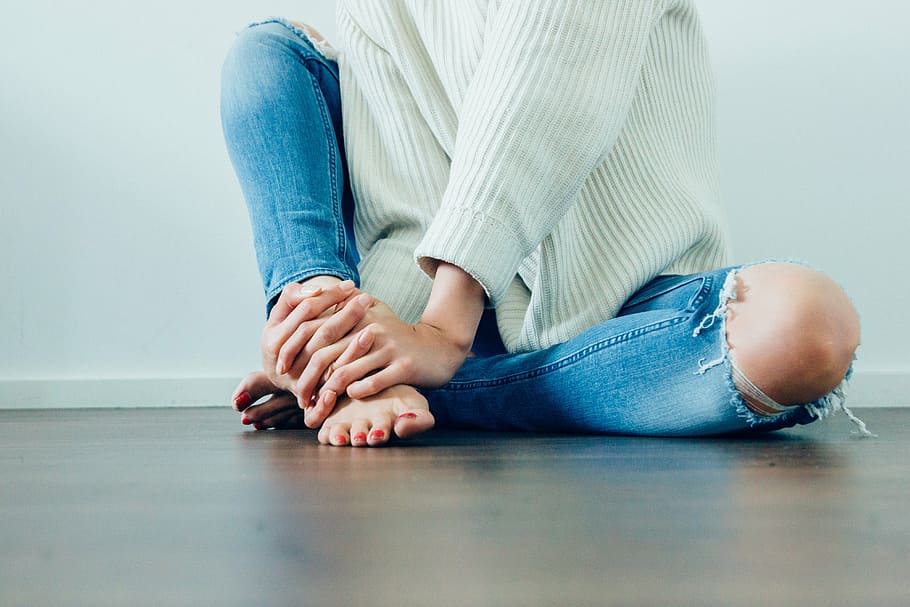 person holding right foot, wearing, distressed, jeans, woman