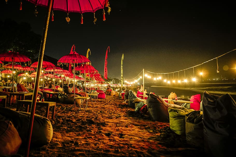 red umbrellas and yellow lights on shore, photo of red parasols near garbage bags and body of water photo taken during nighttime