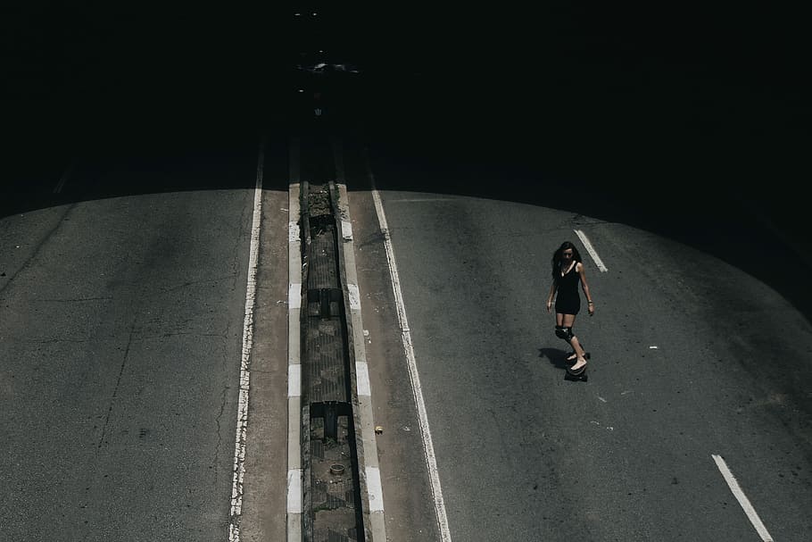 high angle photo of woman riding on skateboard passing road, woman playing skateboard on asphalt road during daytime