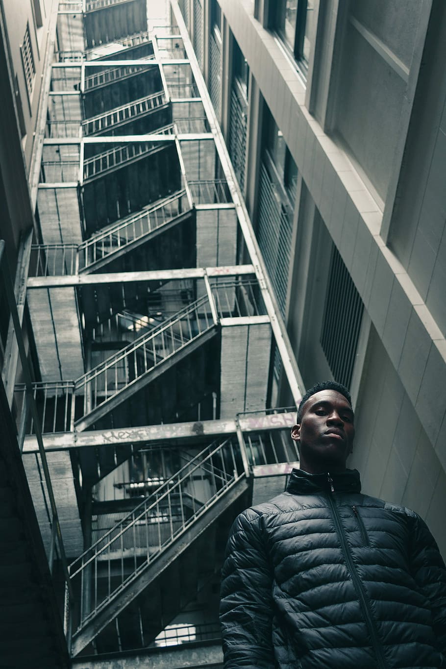 worm's eye view photography of man standing in front of white building, man wearing black bubble jacket standing in between high rise buildings HD wallpaper