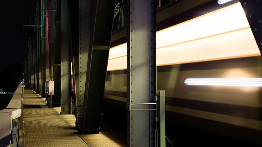 time-lapse photography of a train, gray metal walkway with metal pillars during nighttime HD wallpaper