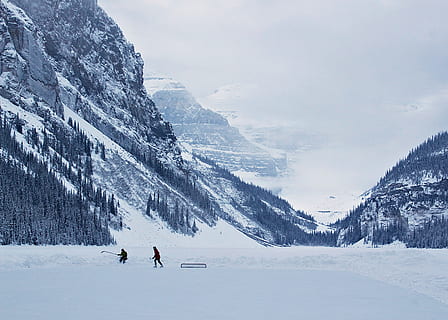 Hockey on Lake Louise, two person playing on snowfield near snow covered mountains at daytime HD wallpaper