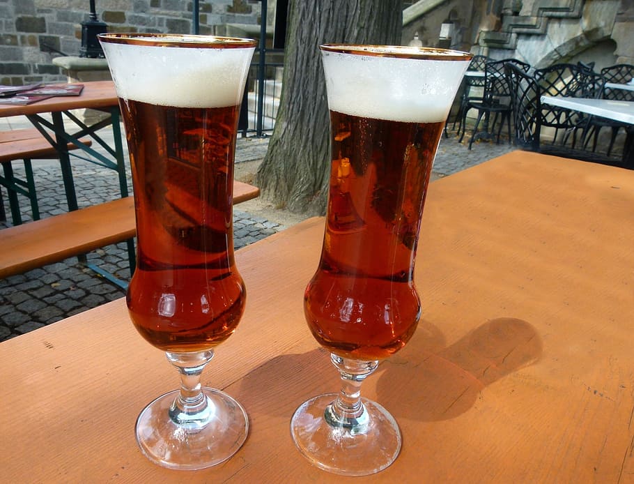two clear glass footed cups with red liquid on table, glasses