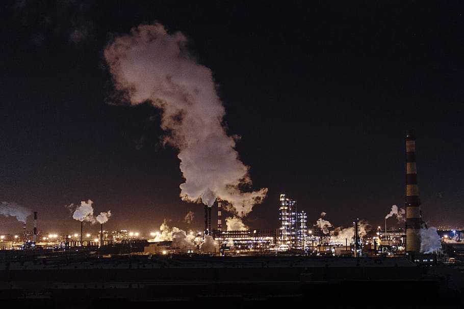 city factories with grey smoke during nighttime, brown and beige concrete factory produces smokes at nighttime