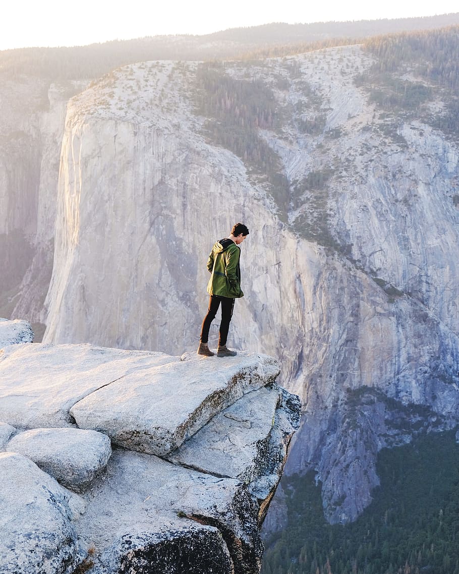 standing man looking on cliff at daytime, man standing on cliff on rock HD wallpaper