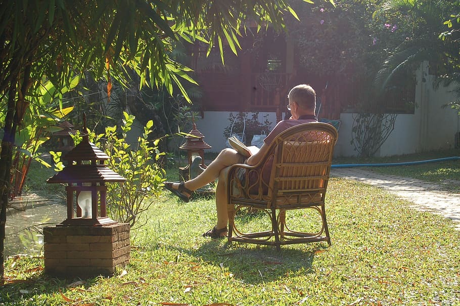 man sitting on armchair in garden during daytime, reading, contemplative HD wallpaper