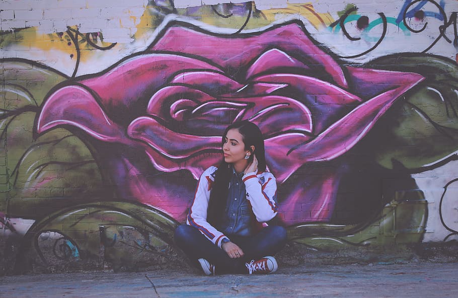 woman sitting beside purple flower wall painting, woman sitting in front of purple flower wall graffiti