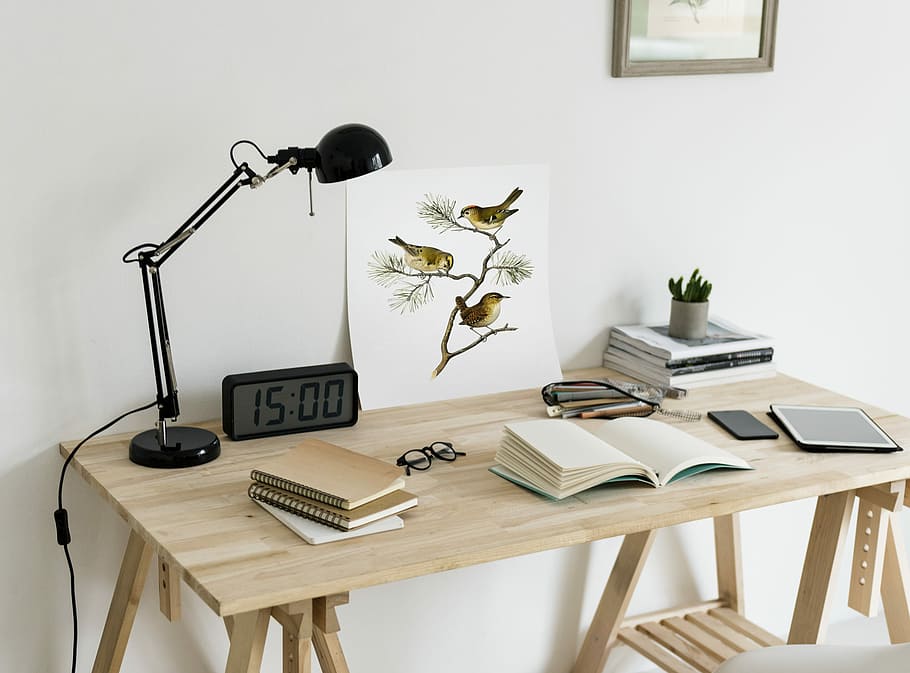 brown wooden desk with lamp, digital clock, painting of three birds perched on twigs and books