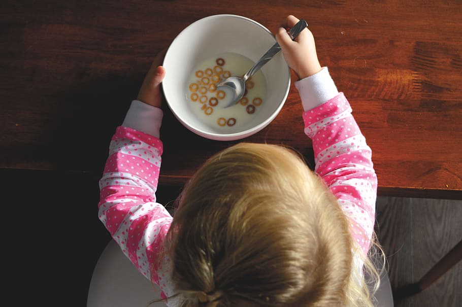 girl eating cereal in white ceramic bowl on table, baby holding spoon eating inside room HD wallpaper