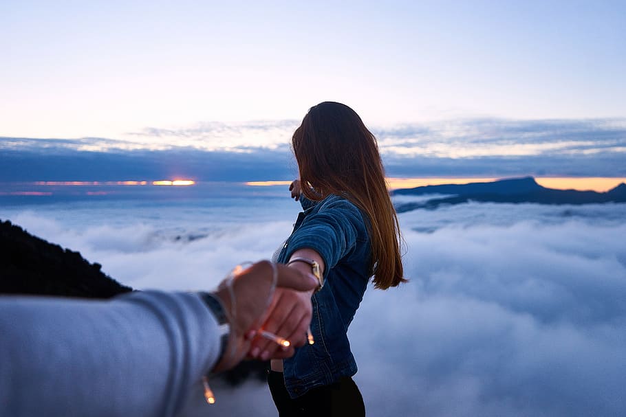 man holding woman's hand on top of mountain, clouds, sky, people
