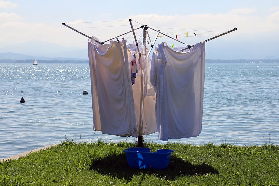 white apparels hanging beside body of water, clothes drying rack
