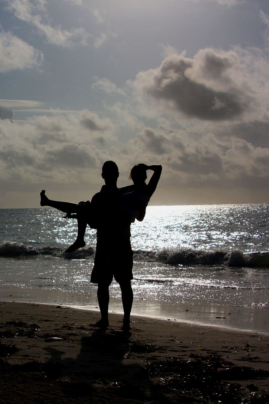 silhouette of man carrying woman near the seashore during sunset