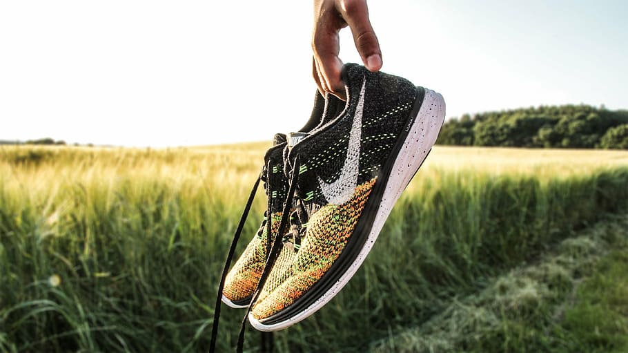 person holding pair of black-and-yellow Nike running shoes, countryside, HD wallpaper