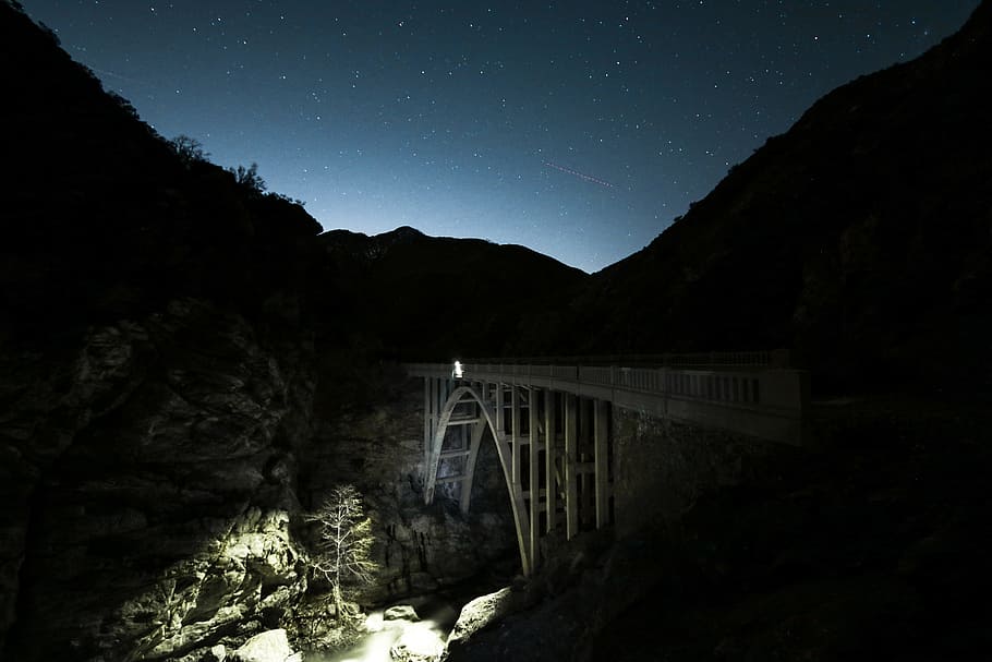 gray bridge under night sky, white concrete bridge over silhouette of mountain under blue sky at night HD wallpaper