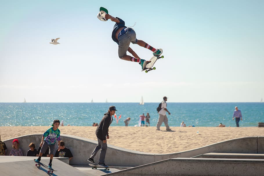 three people playing skateboard beside seashore during daytime, people playing skateboards near body of water during daytime