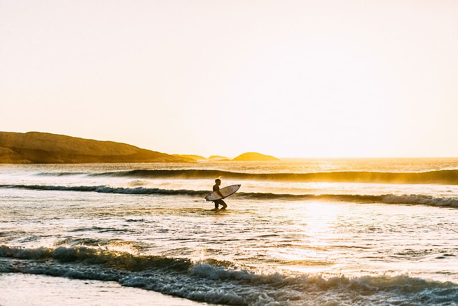 man holding his surfboard, person holding white surfboard on body of water HD wallpaper