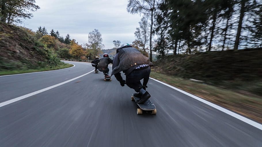three person riding skateboards downhill during daytime, group of people riding longboard on road
