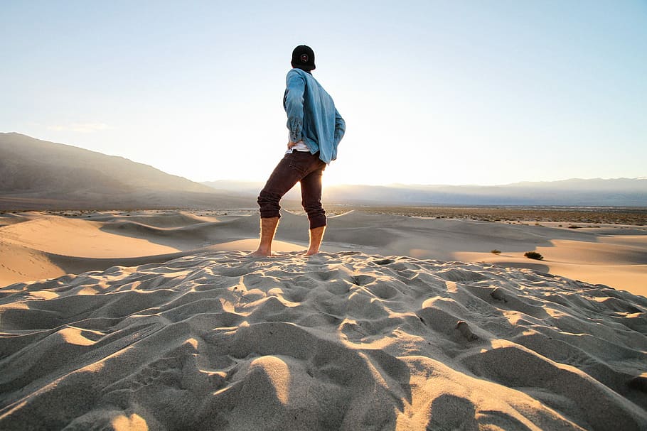 person standing at sand wearing black pants and teal jacket, man standing on sand HD wallpaper