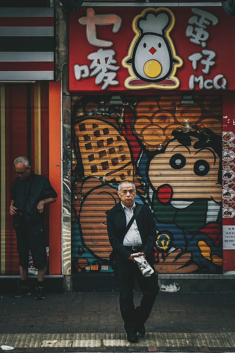 man standing on street in front of red store, man wearing black jacket and black pants walking on gray concrete street at daytime HD wallpaper