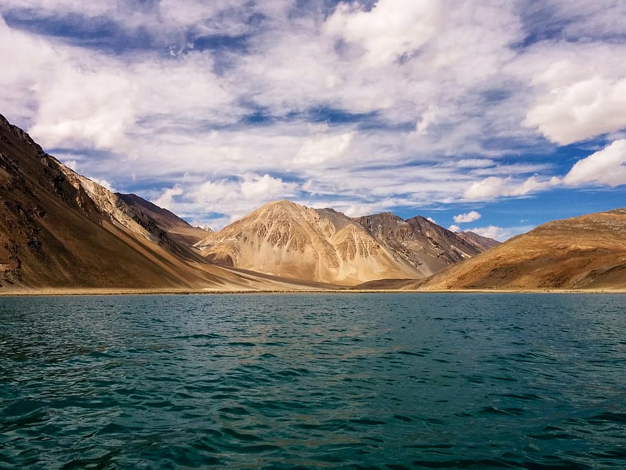 body of water overlooking brown mountain under blue sky at daytime HD wallpaper