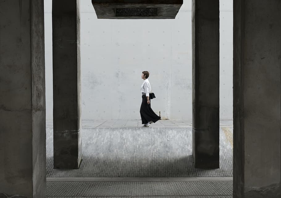 woman walking under a concrete bridge during daytime, woman in white and black long-sleeved dress standing near wall during daytime HD wallpaper