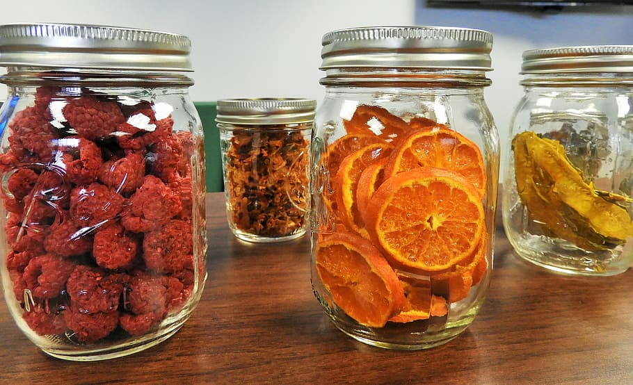 four clear glass mason jars filled with fruits, dehydrated, oranges