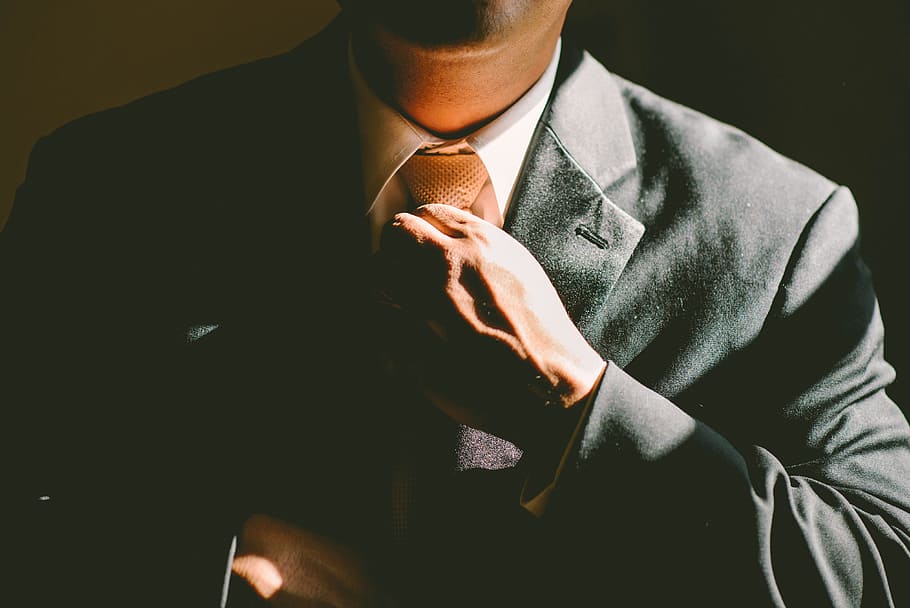 A man in a black suit loosening his tie, man wearing black suit jacket fixing his necktie