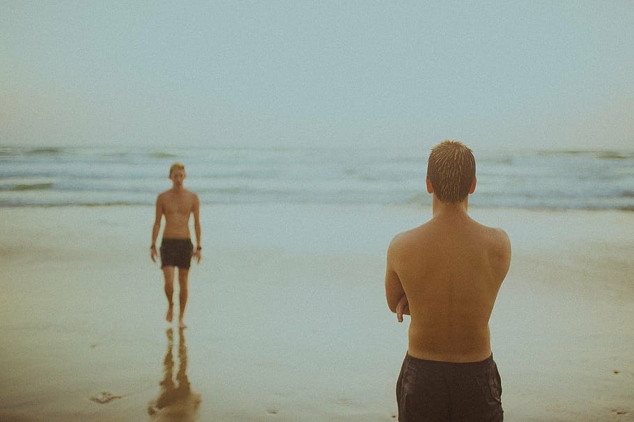 two men wears black shorts stands at seashore, people, beach