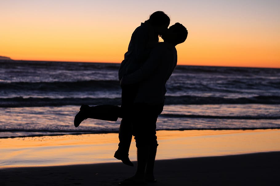 silhouette of kissing coupe near shore of sea during golden hour HD wallpaper