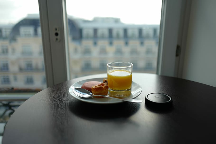 cup filled with yellow liquid beside bread on plate, selective focus photography of glass of tea and bread on plate HD wallpaper