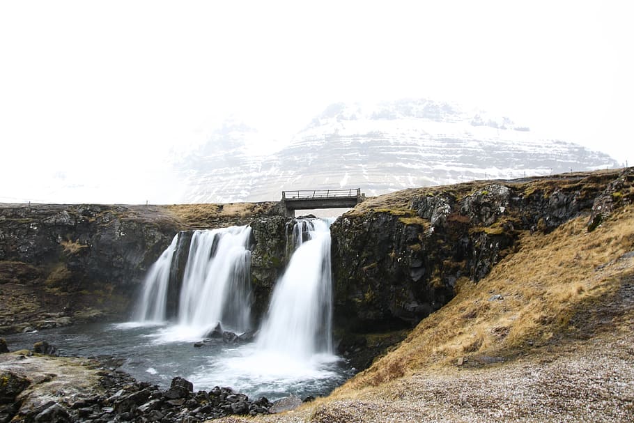 waterfalls near snow-covered mountain at daytime, water flowing on dam under sky at daytime HD wallpaper